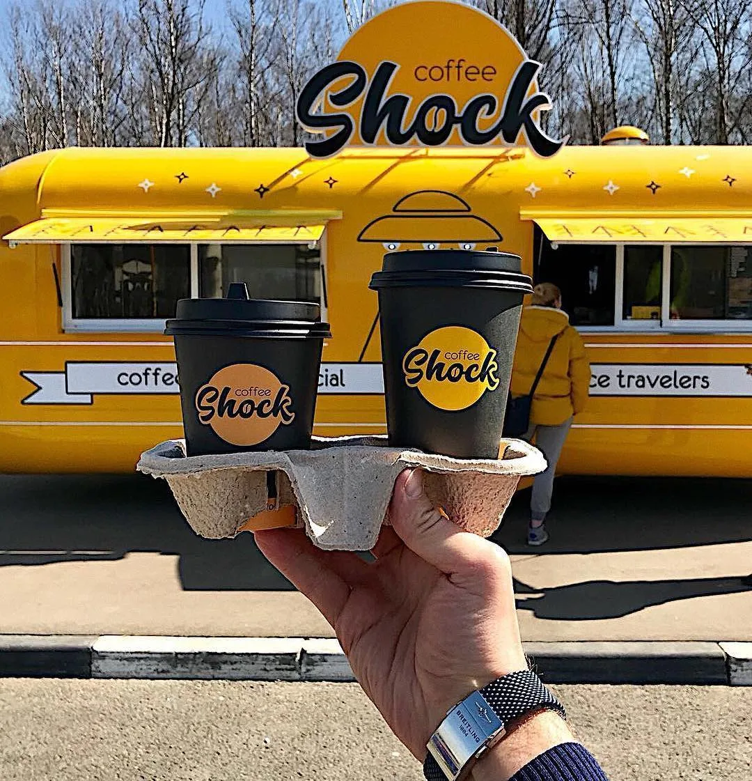Coffee Shock drinks held in front of a yellow MobiEdge 8 coffee trailer