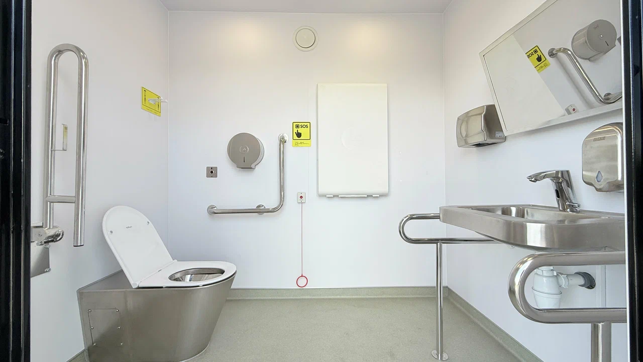Mobile restroom interior with support rails, fold-down station, stainless sink and toilet