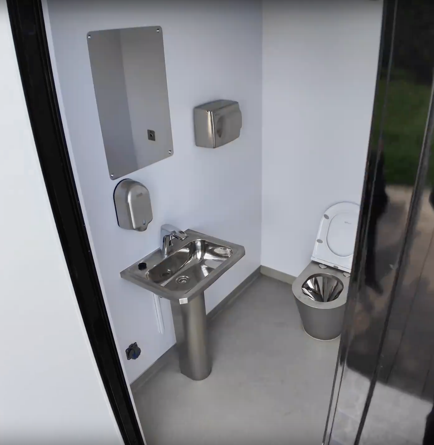 Compact MobiRestroom interior with stainless-steel sink, mirror and toilet viewed through the doorway